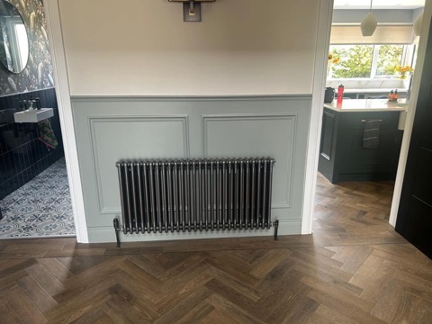 Dark column radiator against a panelled wall with herringbone flooring